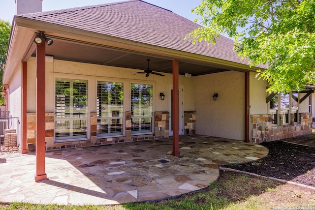 exterior space featuring stone siding, a patio area, a ceiling fan, and roof with shingles
