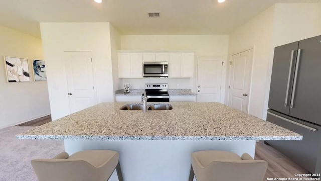kitchen featuring a sink, white cabinetry, light stone countertops, appliances with stainless steel finishes, and a center island with sink