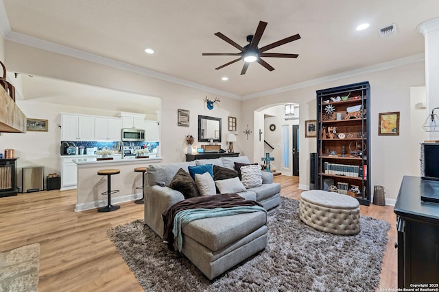 living room with crown molding, a ceiling fan, light wood-type flooring, visible vents, and arched walkways