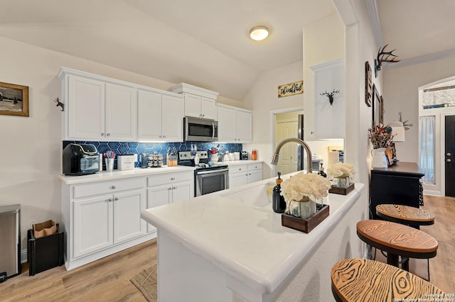 kitchen featuring vaulted ceiling, white cabinets, decorative backsplash, and stainless steel appliances