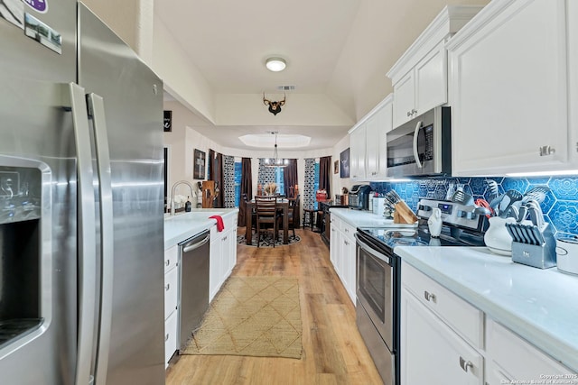kitchen with light countertops, a raised ceiling, tasteful backsplash, appliances with stainless steel finishes, and light wood-type flooring