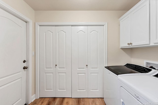 clothes washing area featuring light wood-style flooring, washing machine and clothes dryer, and cabinet space