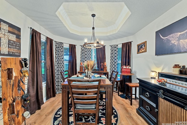 dining space with a tray ceiling, a notable chandelier, light wood-style floors, and a textured ceiling