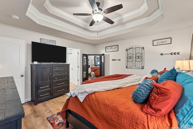 bedroom featuring a tray ceiling, crown molding, light wood-style flooring, and a ceiling fan