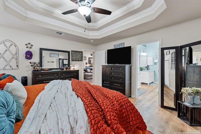 bedroom with a tray ceiling, visible vents, light wood-type flooring, and ornamental molding