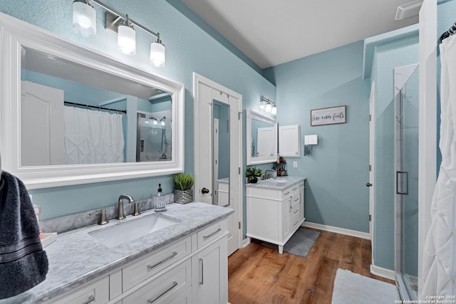 full bathroom with a sink, a stall shower, two vanities, and wood finished floors