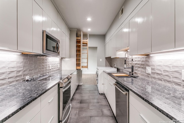 kitchen with stainless steel appliances, tile patterned floors, dark stone countertops, white cabinetry, and a sink
