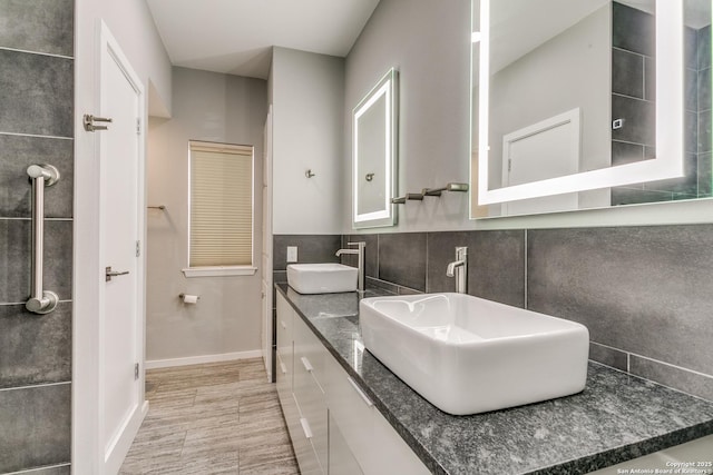 full bathroom featuring tile walls, double vanity, a sink, and baseboards