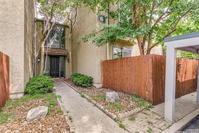 view of exterior entry with stucco siding and fence