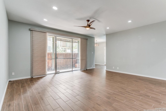 spare room featuring recessed lighting, ceiling fan with notable chandelier, baseboards, and wood finished floors