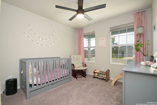 carpeted bedroom featuring baseboards, a ceiling fan, and a nursery area