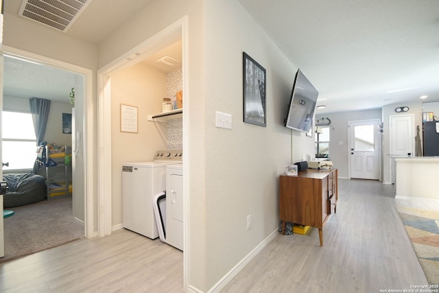 corridor with visible vents, separate washer and dryer, light wood-type flooring, and plenty of natural light