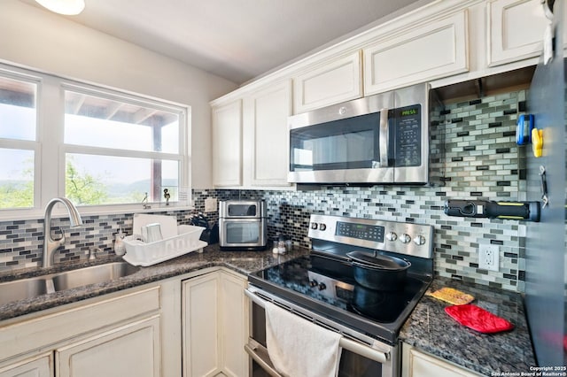 kitchen featuring backsplash, a sink, appliances with stainless steel finishes, and dark stone counters
