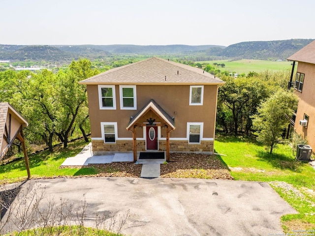 view of front of property featuring stucco siding, central air condition unit, stone siding, a mountain view, and a shingled roof