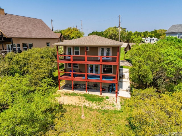 rear view of property with a balcony, roof with shingles, and a patio