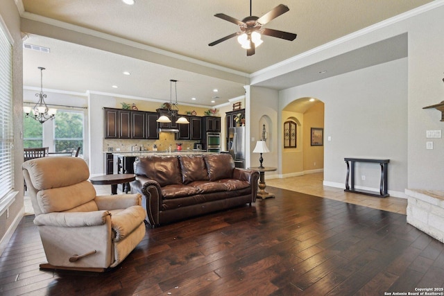living room featuring arched walkways, ornamental molding, light wood-type flooring, ceiling fan with notable chandelier, and visible vents