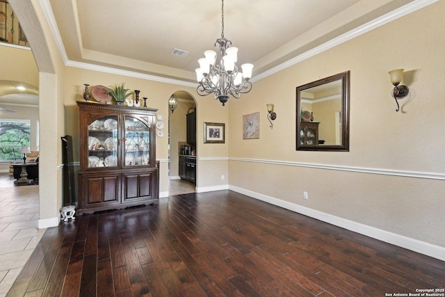 interior space with a raised ceiling, visible vents, arched walkways, an inviting chandelier, and wood finished floors