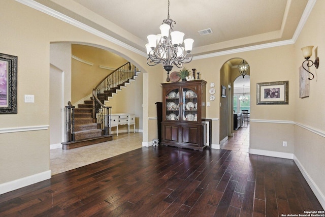 entryway with stairway, a chandelier, a tray ceiling, arched walkways, and wood finished floors