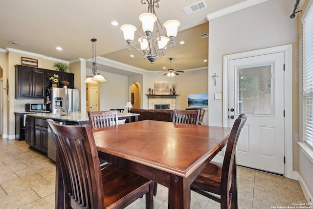 dining space featuring visible vents, arched walkways, recessed lighting, a stone fireplace, and ceiling fan with notable chandelier