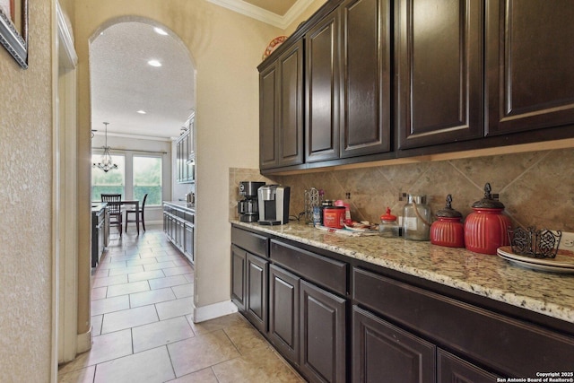 kitchen featuring tasteful backsplash, dark brown cabinets, crown molding, and light tile patterned floors