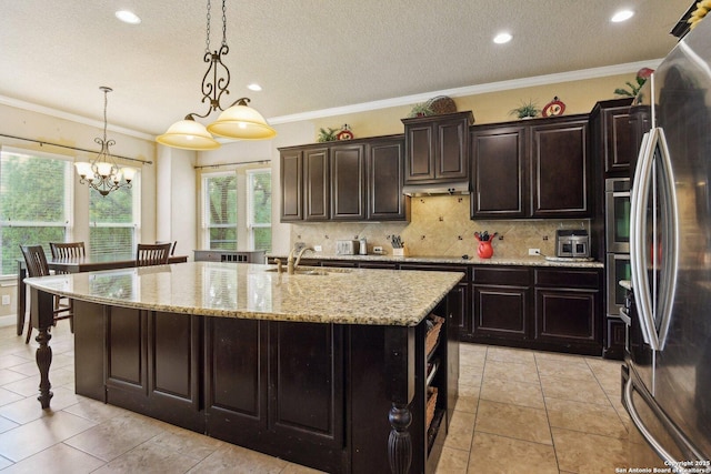kitchen with a kitchen island with sink, light stone counters, decorative backsplash, freestanding refrigerator, and a sink