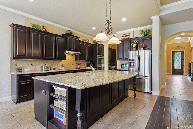 kitchen with tasteful backsplash, open shelves, appliances with stainless steel finishes, arched walkways, and a center island with sink