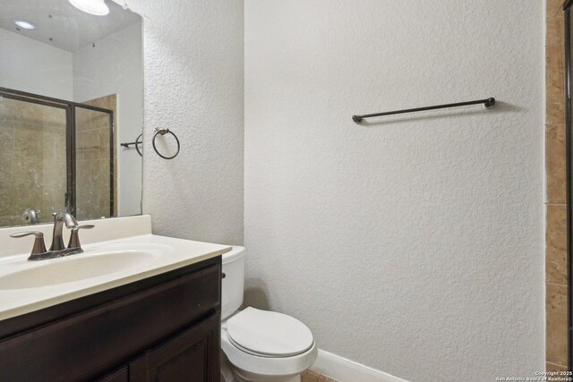bathroom featuring toilet, a textured wall, a shower stall, and vanity