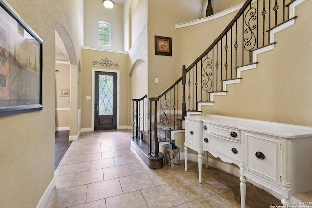 entryway featuring tile patterned floors, stairs, baseboards, a towering ceiling, and arched walkways