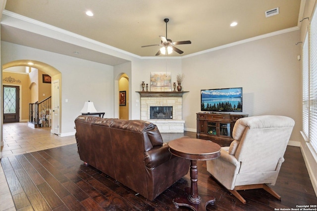 living area with visible vents, dark wood-style floors, arched walkways, a fireplace, and a ceiling fan