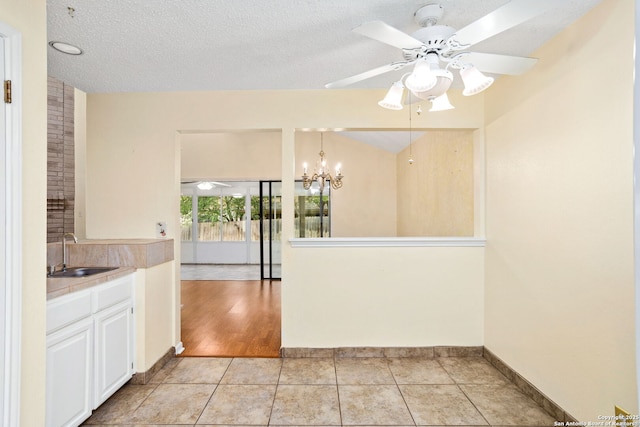 kitchen featuring light countertops, white cabinets, a sink, ceiling fan with notable chandelier, and light tile patterned floors