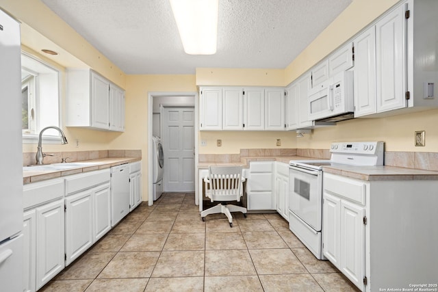 kitchen with white appliances, light tile patterned floors, a sink, washer / clothes dryer, and white cabinets