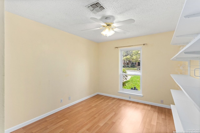 empty room with a textured ceiling, light wood-style flooring, visible vents, baseboards, and a ceiling fan
