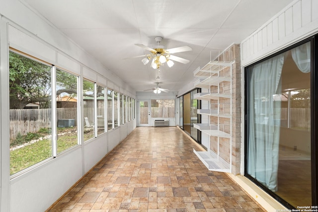 unfurnished sunroom with a ceiling fan, stone finish flooring, and a wall mounted air conditioner