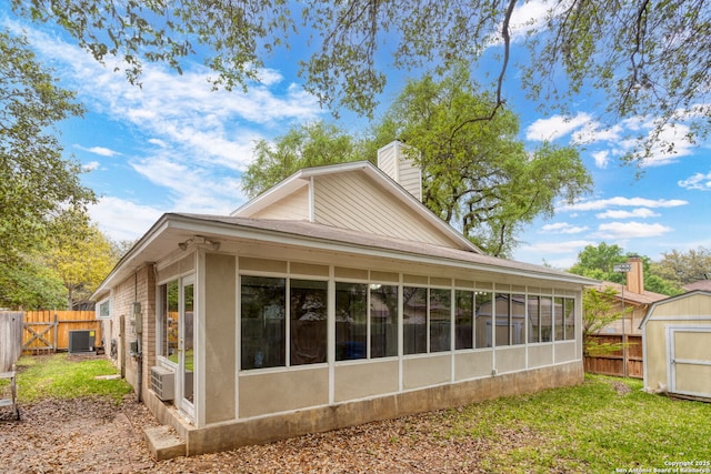 view of side of home featuring a shed, cooling unit, an outbuilding, a fenced backyard, and a sunroom