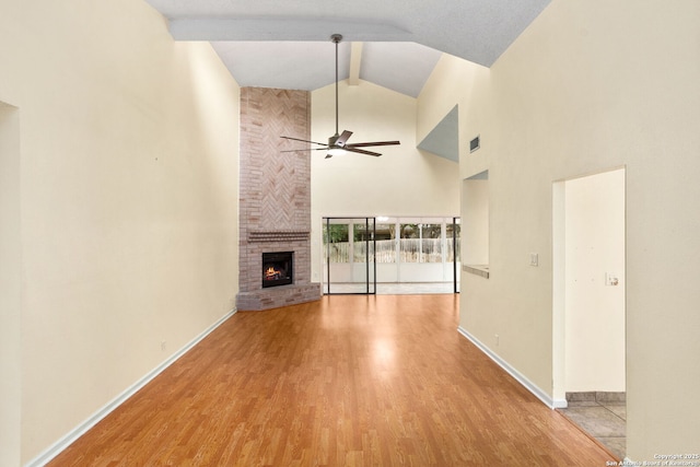unfurnished living room with a ceiling fan, a fireplace, wood finished floors, baseboards, and beamed ceiling