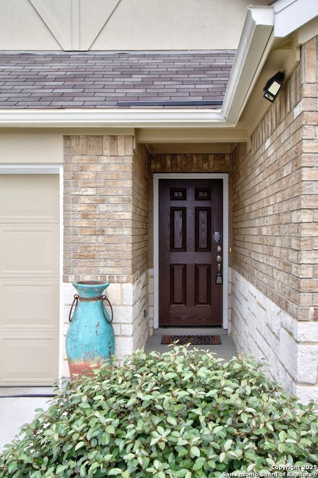 property entrance with stone siding, a garage, brick siding, and roof with shingles