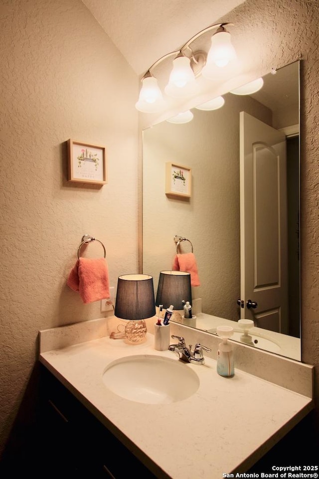 bathroom featuring vanity, a textured wall, and lofted ceiling