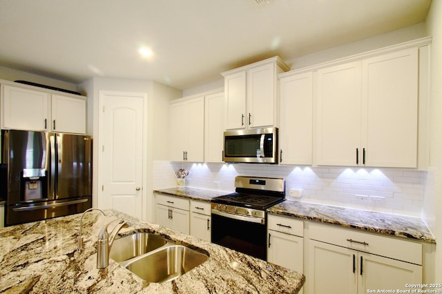 kitchen with light stone counters, a sink, backsplash, stainless steel appliances, and white cabinets