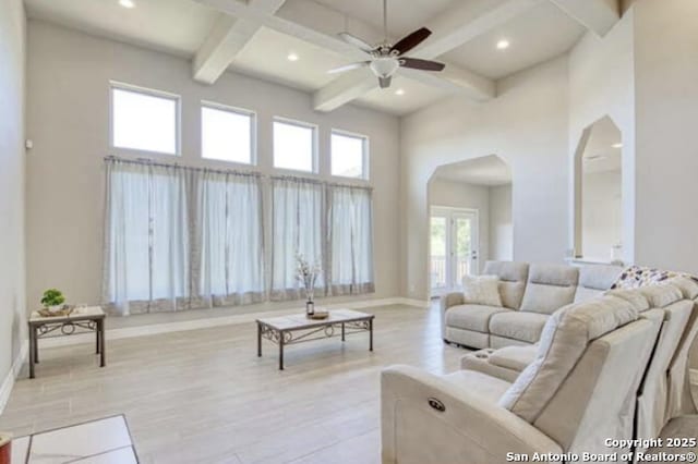 living area with beam ceiling, a towering ceiling, arched walkways, and a ceiling fan