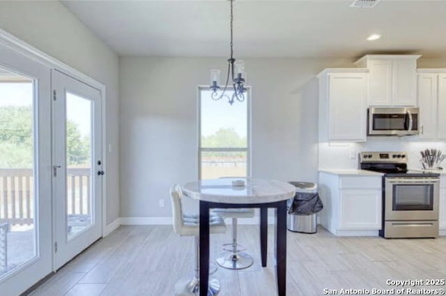 kitchen with appliances with stainless steel finishes, a chandelier, white cabinetry, and plenty of natural light