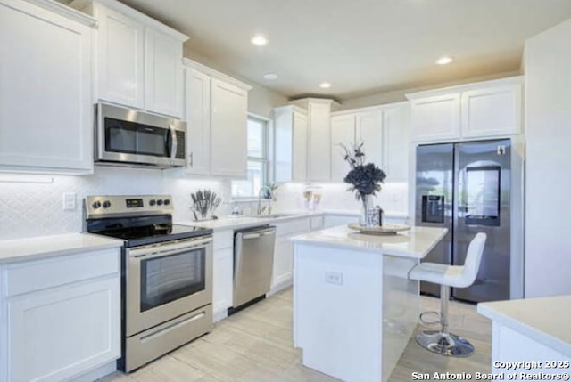 kitchen featuring a center island, a breakfast bar, light countertops, white cabinets, and appliances with stainless steel finishes