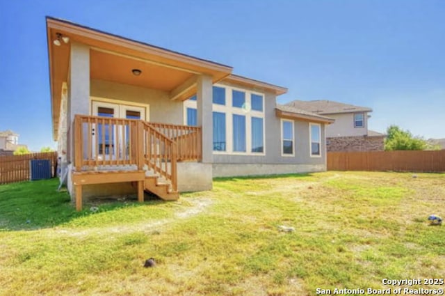 back of property with fence, a lawn, central air condition unit, and stucco siding