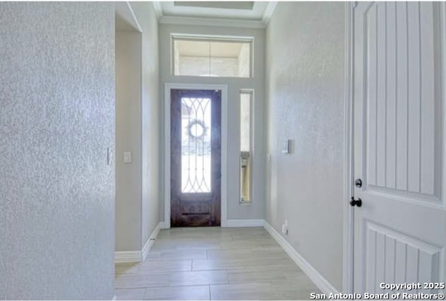 foyer entrance with baseboards, crown molding, and a high ceiling