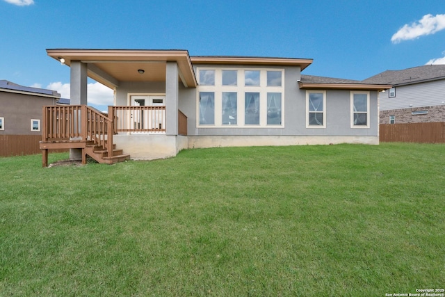 back of property featuring stucco siding, a lawn, and fence