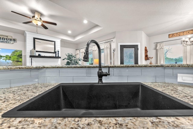 interior details with light stone countertops, a tray ceiling, a ceiling fan, recessed lighting, and a sink
