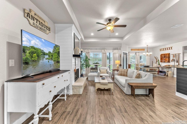 living room featuring a raised ceiling, wood finished floors, ceiling fan with notable chandelier, and a fireplace
