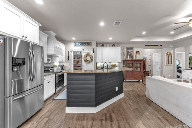 kitchen with visible vents, premium range hood, wood finished floors, and stainless steel appliances
