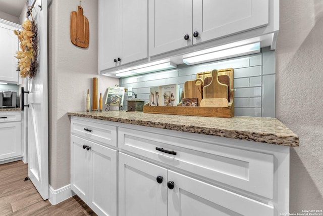kitchen with a textured wall, decorative backsplash, white cabinets, light stone counters, and light wood finished floors