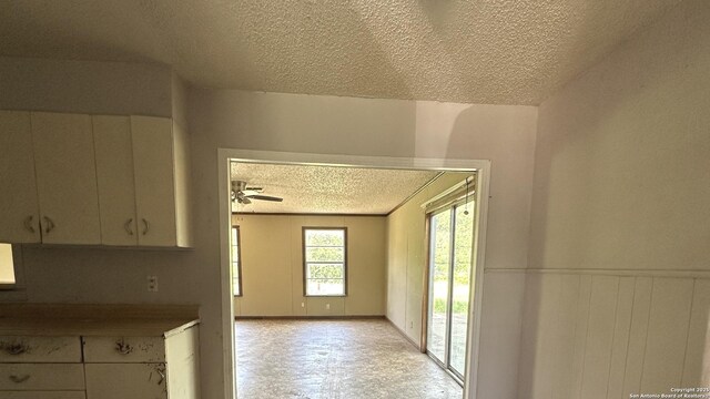 4535 Lark, San Antonio, TX 78228 - kitchen featuring a textured ceiling, white cabinetry, a ceiling fan, light floors, and a wainscoted wall