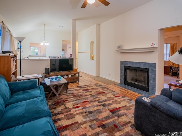 living area with vaulted ceiling, a fireplace, wood finished floors, baseboards, and ceiling fan